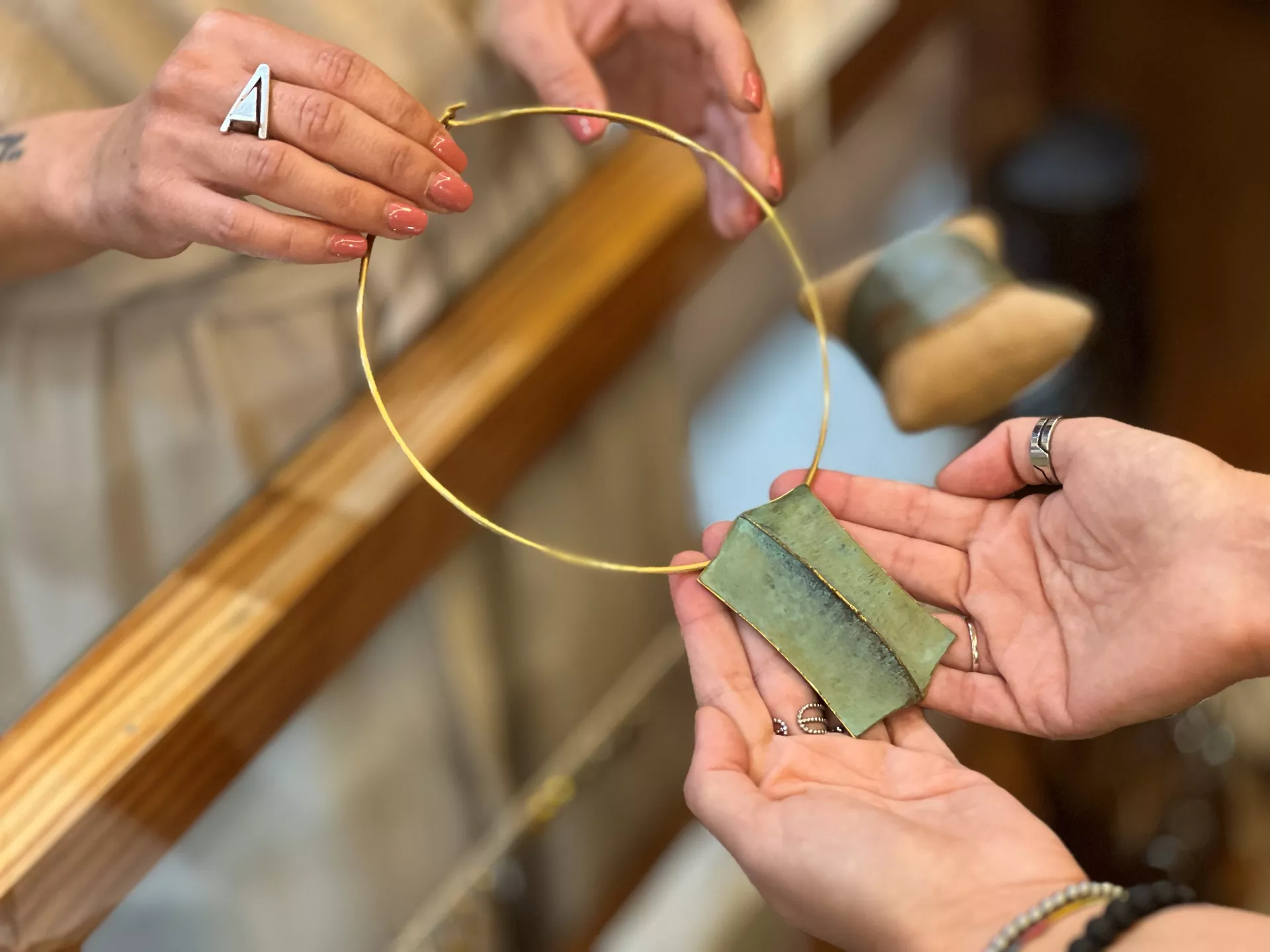 Manos sujetando un collar con aro dorado y colgante con forma de hoja verde